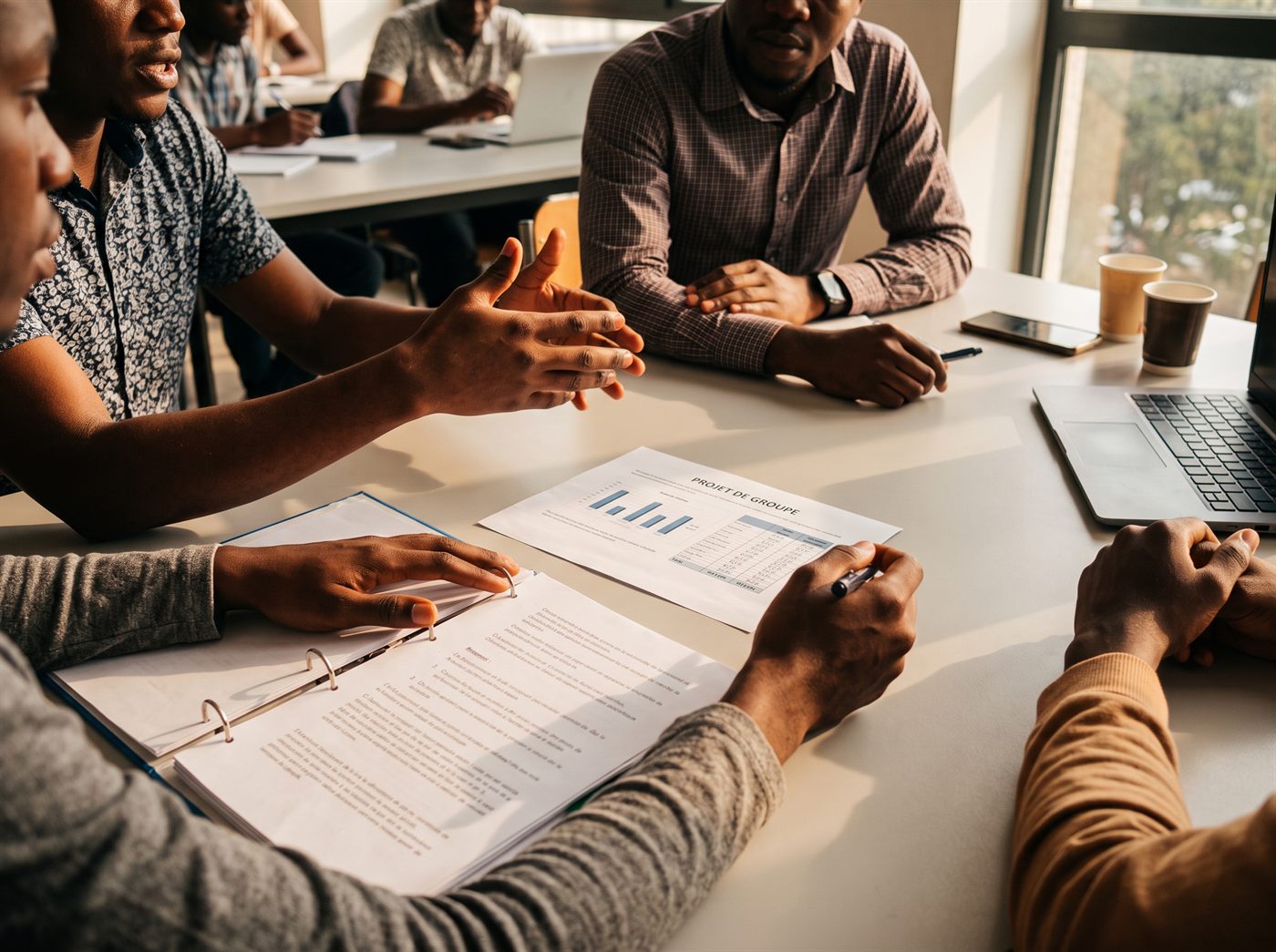 Quatre étudiants discutent autour d’un document de projet posé sur une table de travail.